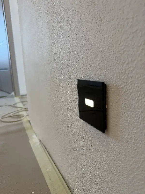 Černý dotykový vypínač s podsvícením na stěně